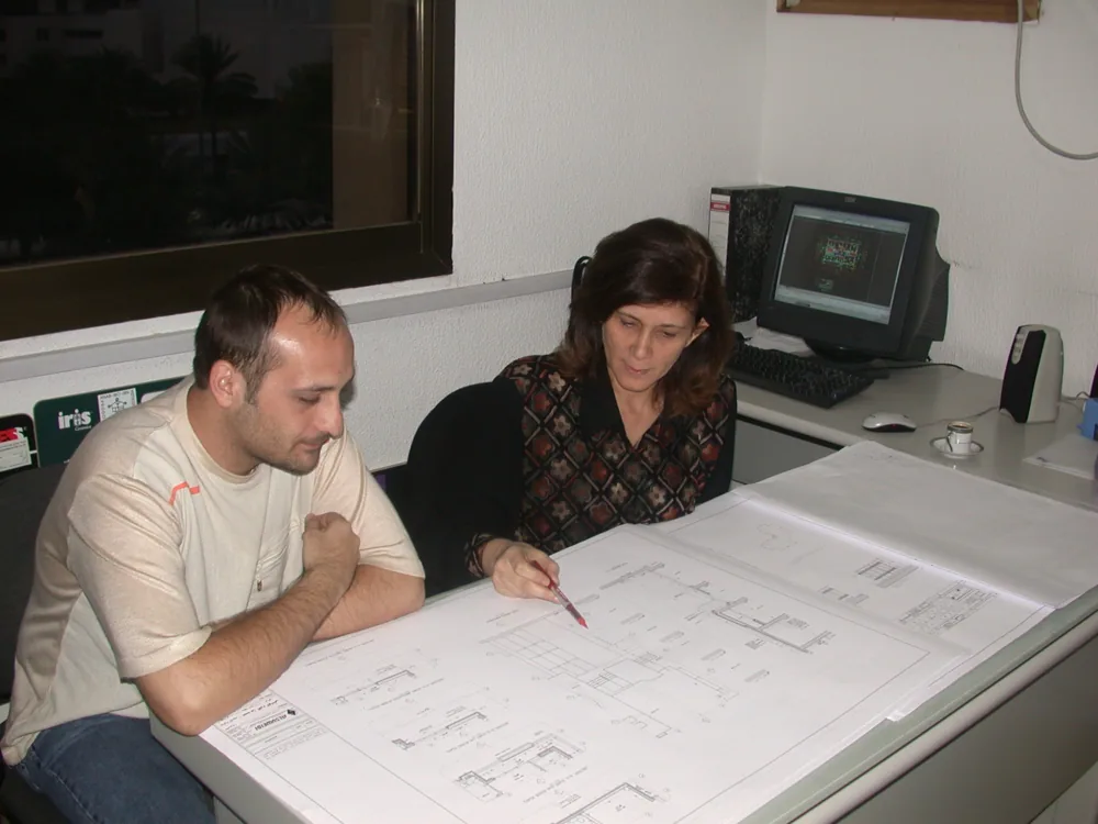Two ALSUWEIDI architects reviewing drawings at the table in the early office